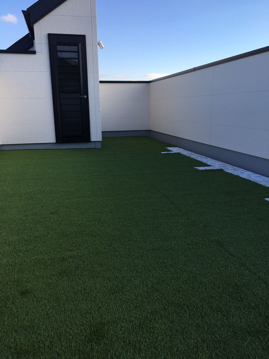 夕方の屋上テラスに施工した人工芝、黒い扉のある建物際まで仕上げ