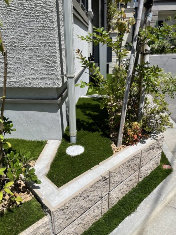 植栽に挟まれた建物際のスペースを境界のブロックに沿って納めた人工芝に｜和歌山管財合同会社様（千葉市）の施工事例