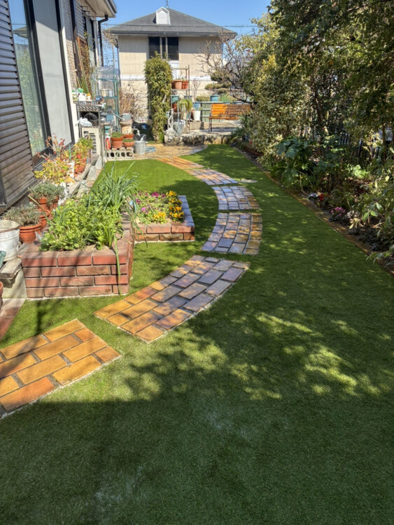 レンガの小道と花壇を残した庭を曲線の際まで合わせた緑に｜大津市の人工芝施工事例
