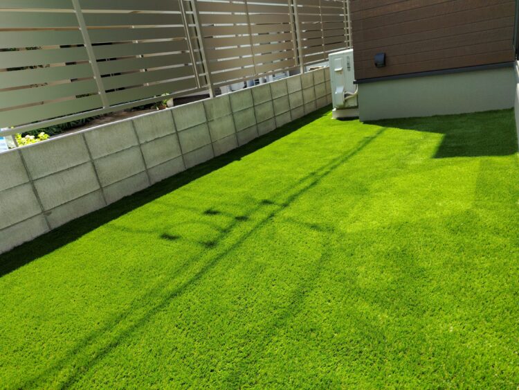 室外機の前まで続く建物脇を塀の際まで隙間なく敷いた緑に｜岡山市の人工芝施工事例