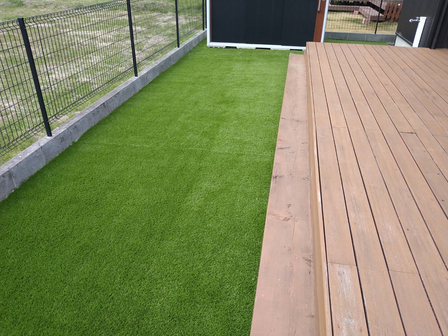 施工後:フェンス際とデッキ際まで人工芝を敷いた横長の庭