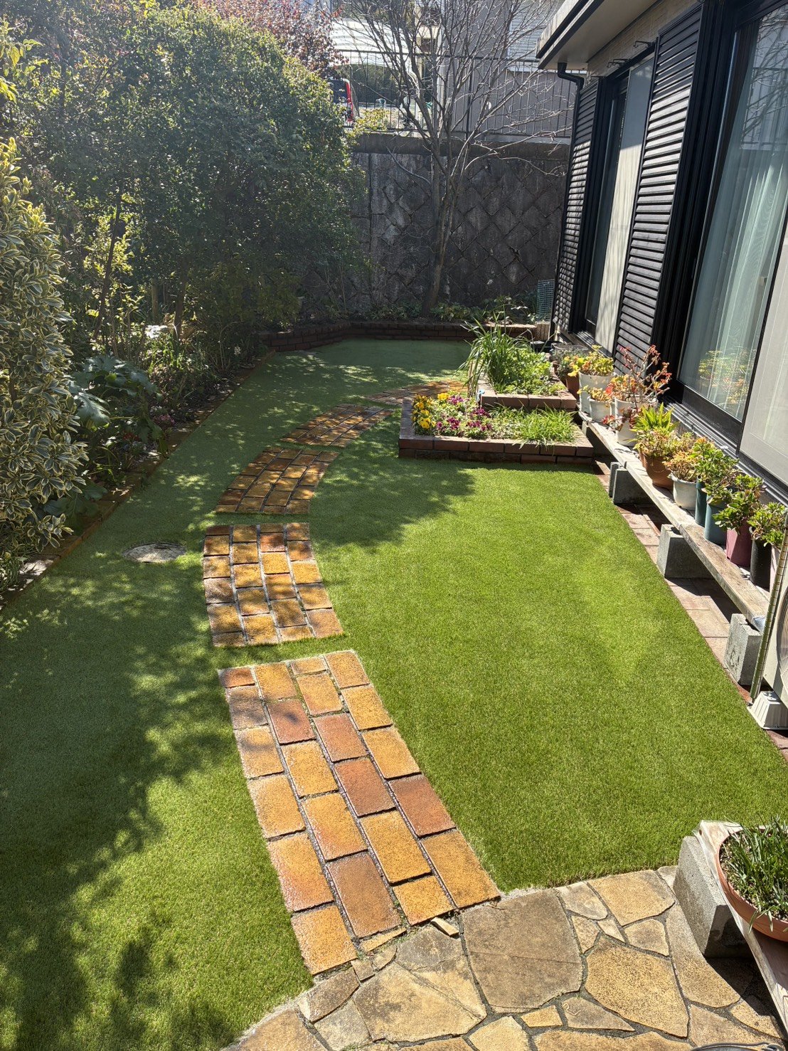 施工後：テラスから見た庭全体の人工芝、鉢植えが並ぶ